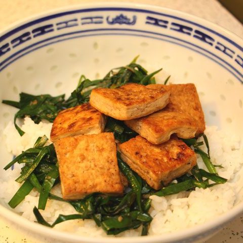fried tofu on a bed of chives and garlic atop white rice in blue and white ceramic bowl.