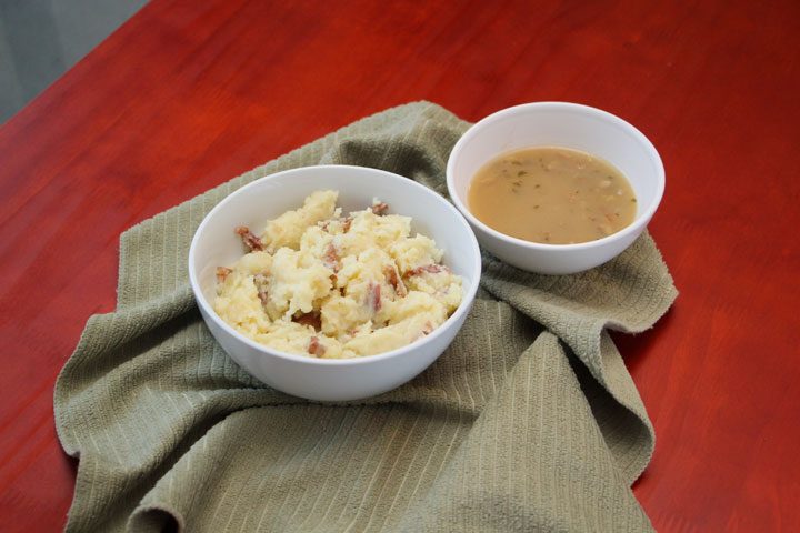 bowl of gravy next to mashed potatoes with gray towel.