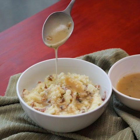 spoon dripping with gravy over bed of mashed potatoes.